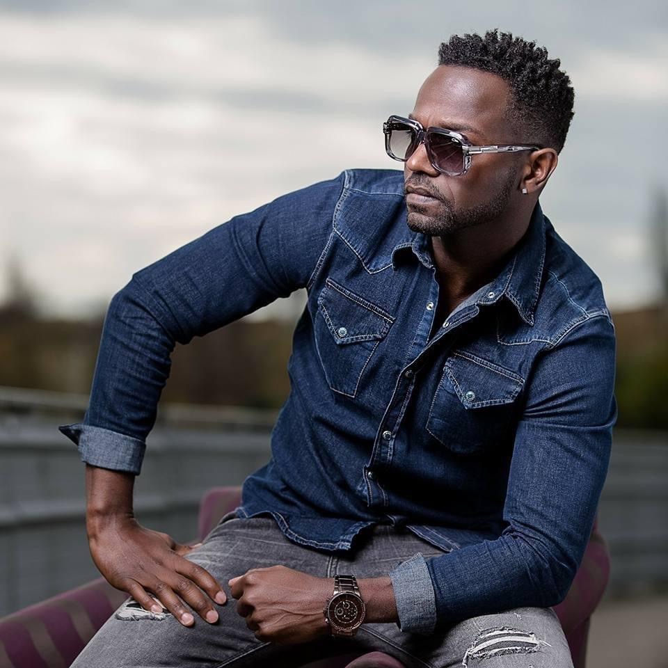 Jaydee Luv en chemise en jean et lunettes de soleil, assis en extérieur